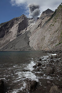 Rocky beach at foot of Batu Tara volcano with eruption