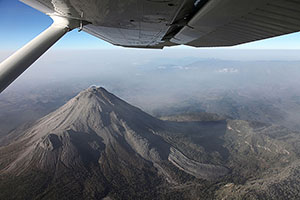 View of Fuego de Colima volcano from aircraft with wing in image, Mexico
