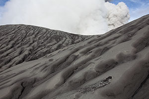 Small impact crater in eroded ash landscape. Dukono volcano summit cone