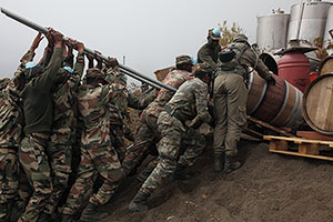 Soldiers sliding wine barrel into place on hillside terrace, Evacuation of Portela, Fogo Eruption 2014