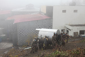 Soldiers carrying fermenter during evacuation of Portelo, Wine co-op building behind