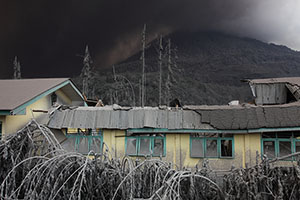 School roof collapsed by volcanic ash load, Sinabung Volcano behind